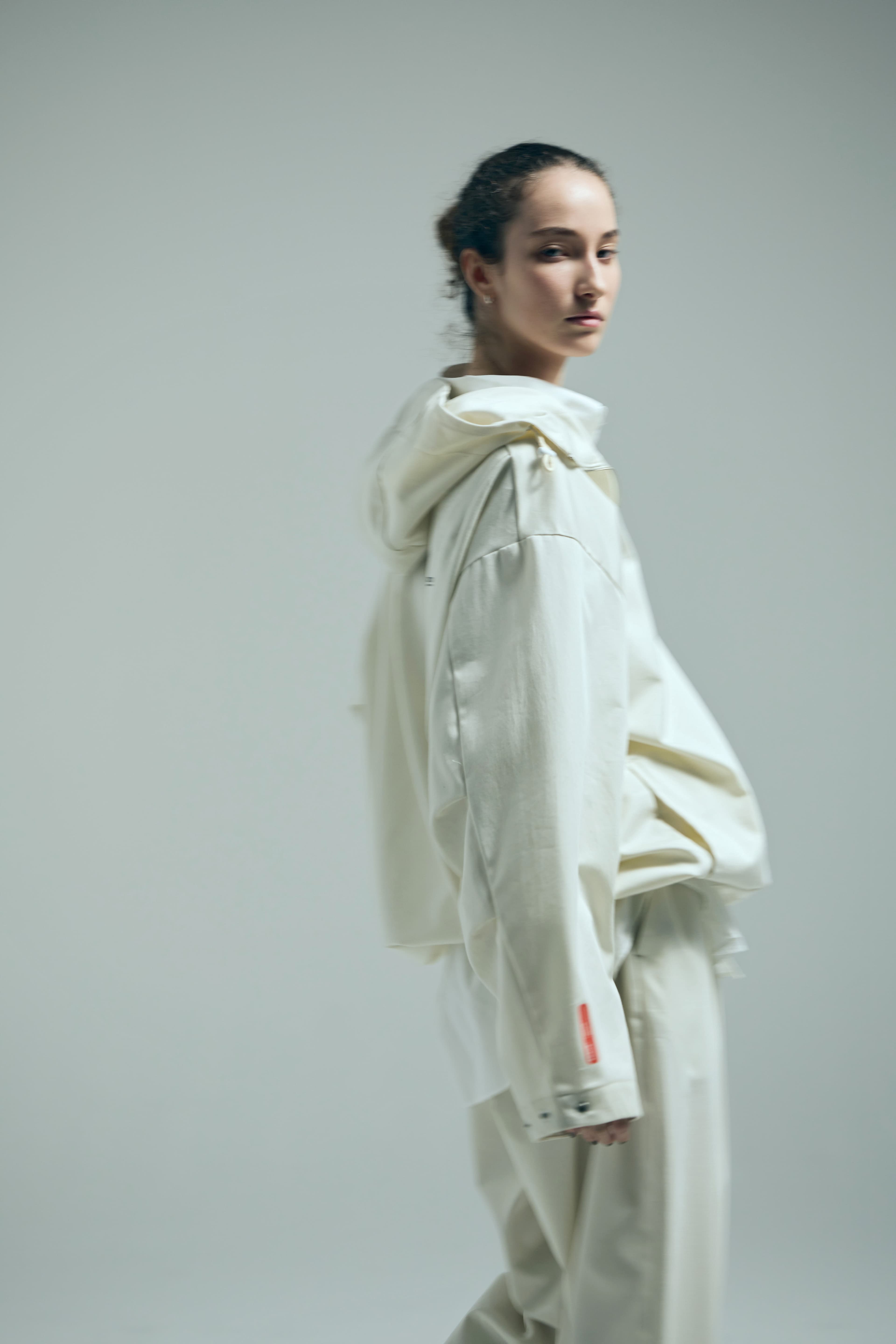 Woman in an oversized cream hooded jacket and matching trousers looking back over her shoulder.