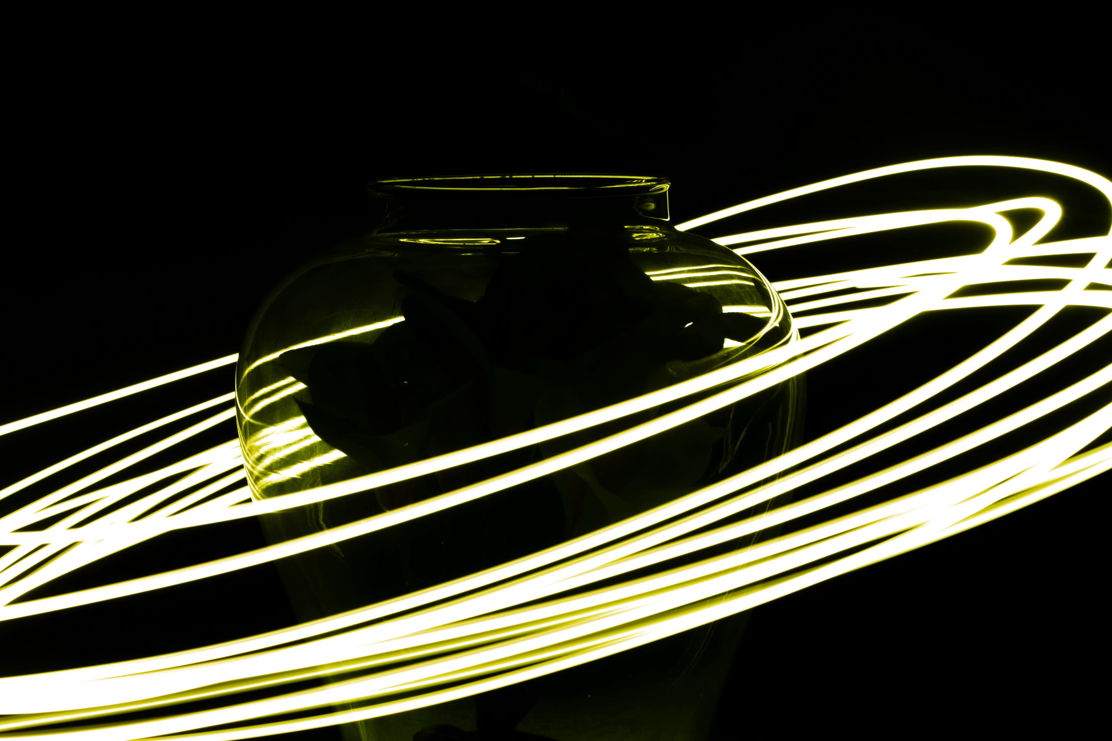 Glowing yellow light streaks spiral around a glass vase against a solid black background.